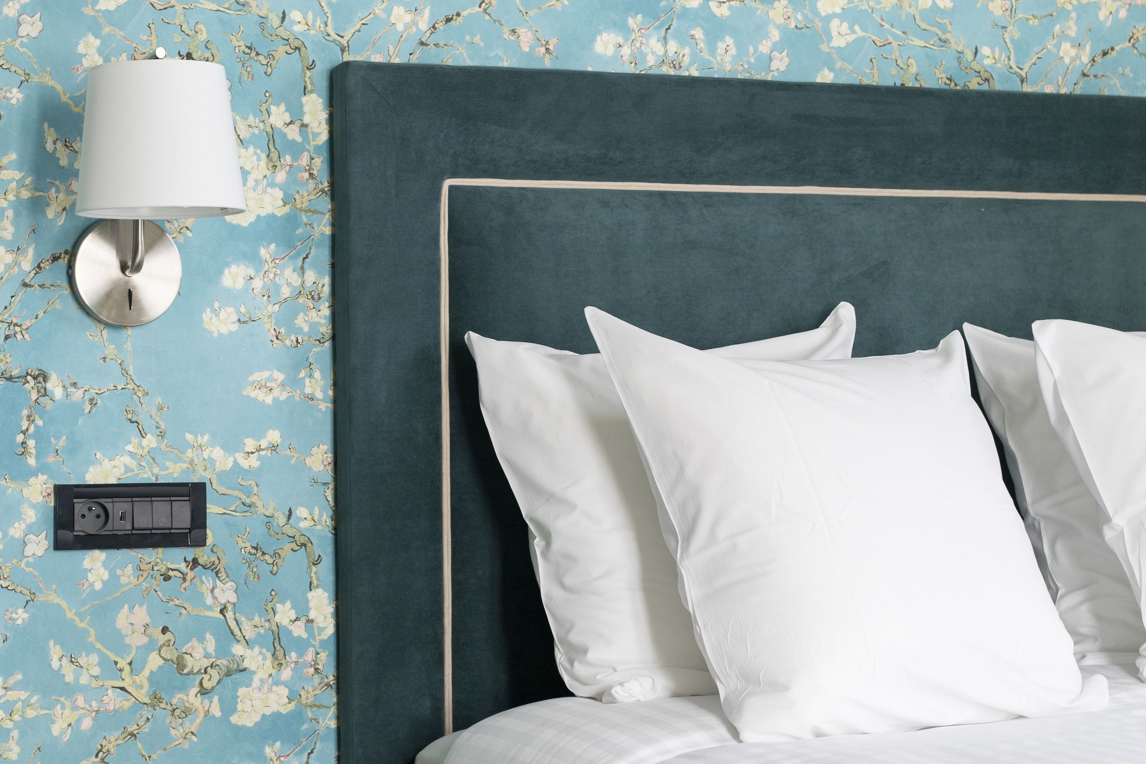 Ein Bett mit weißer Bettwäsche und Kopfteil, eine Wandlampe und eine Steckdose.