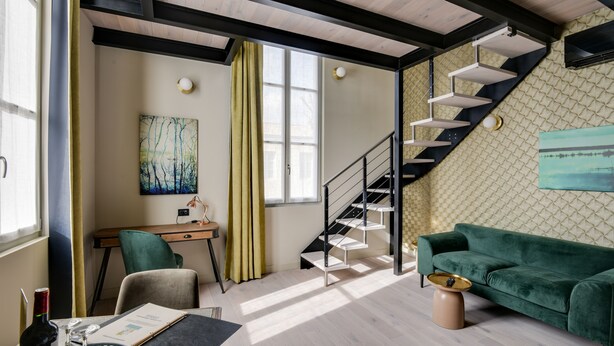 Un salon moderne avec un escalier, un bureau et un canapé vert.
