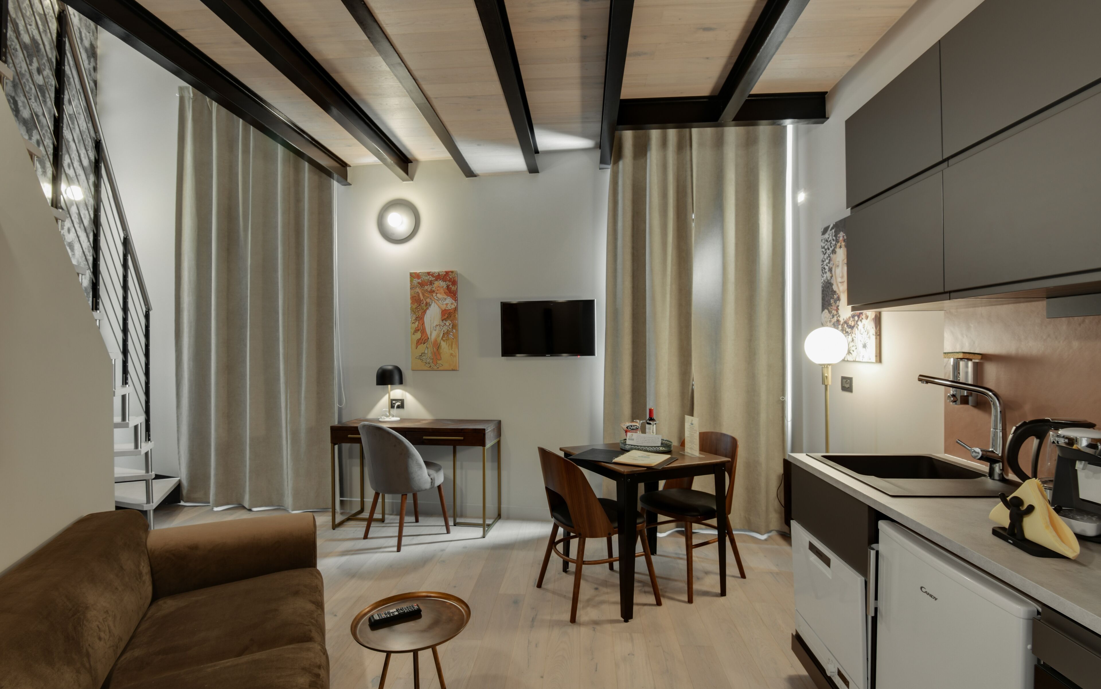 Una sala moderna con un sofá, un comedor con sillas, una cocina con pileta y estufa, y una escalera con cortinas.
