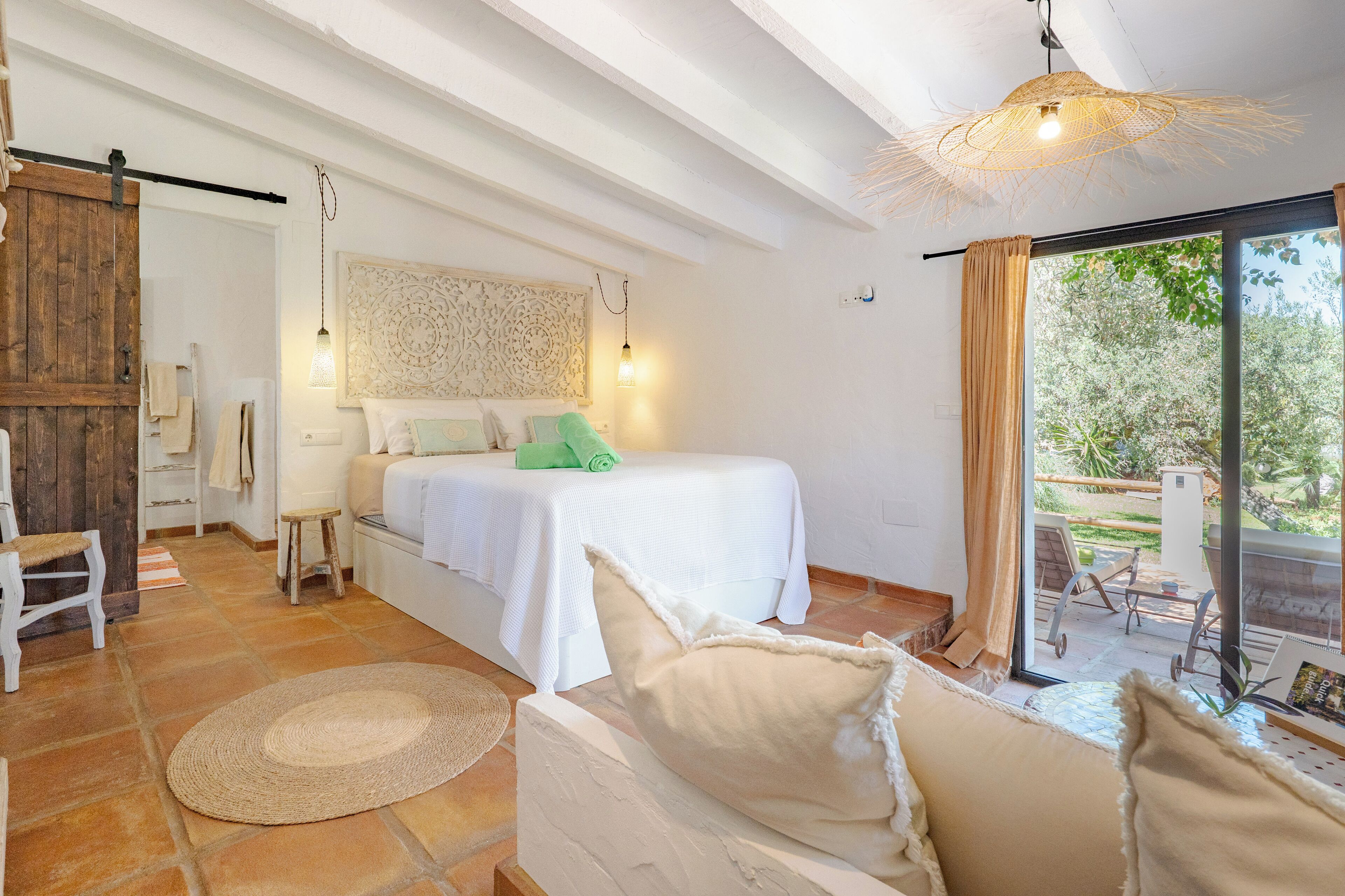 Een slaapkamer met een bed, een witte bank, een groot raam en uitzicht op de omgeving.