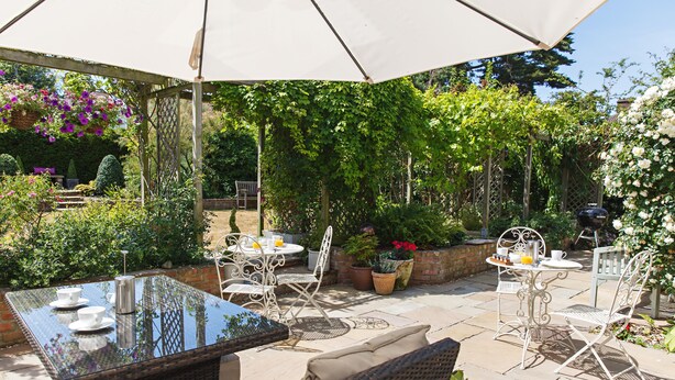 An outdoor patio with a glass-top table, wicker furniture, and potted plants. - Alton House (Sheringham)