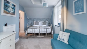 A bedroom with a bed, a dresser, a blue sofa, and a window with curtains. - Alton House (Sheringham)