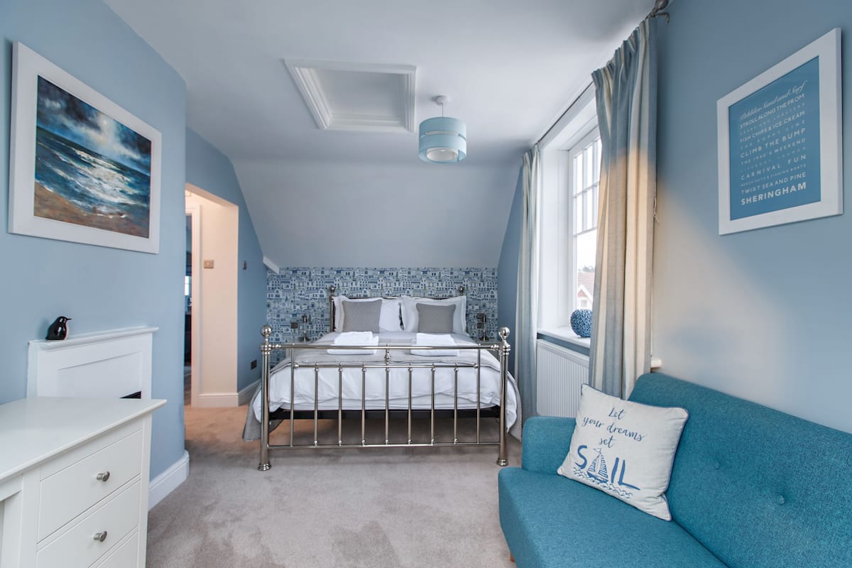 A bedroom with a bed, a dresser, a blue sofa, and a window with curtains.