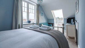 A bedroom with a large bed, a desk, and a view of the city. - Alton House (Sheringham)