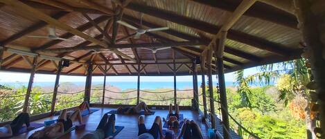 A covered outdoor yoga area with wooden beams and a view of the ocean.