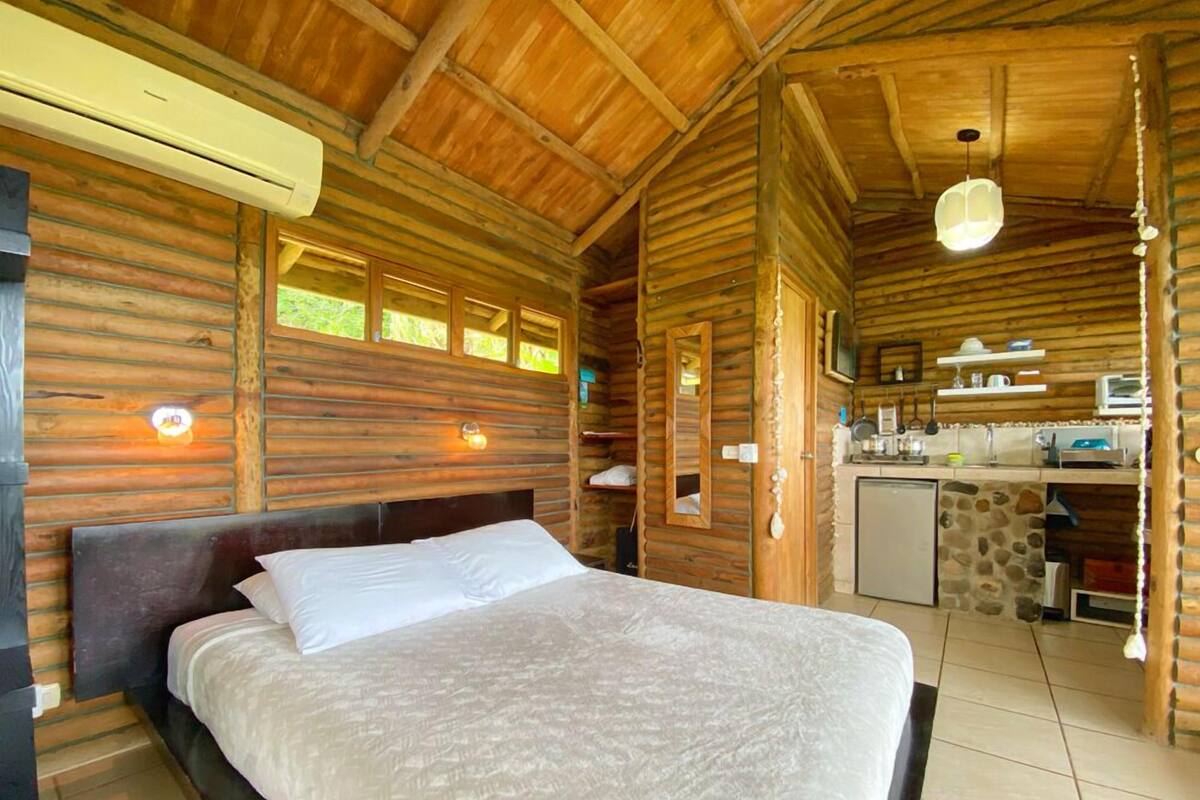 Une chambre située dans un chalet en rondins, avec un lit, une petite kitchenette et un mur en pierre.