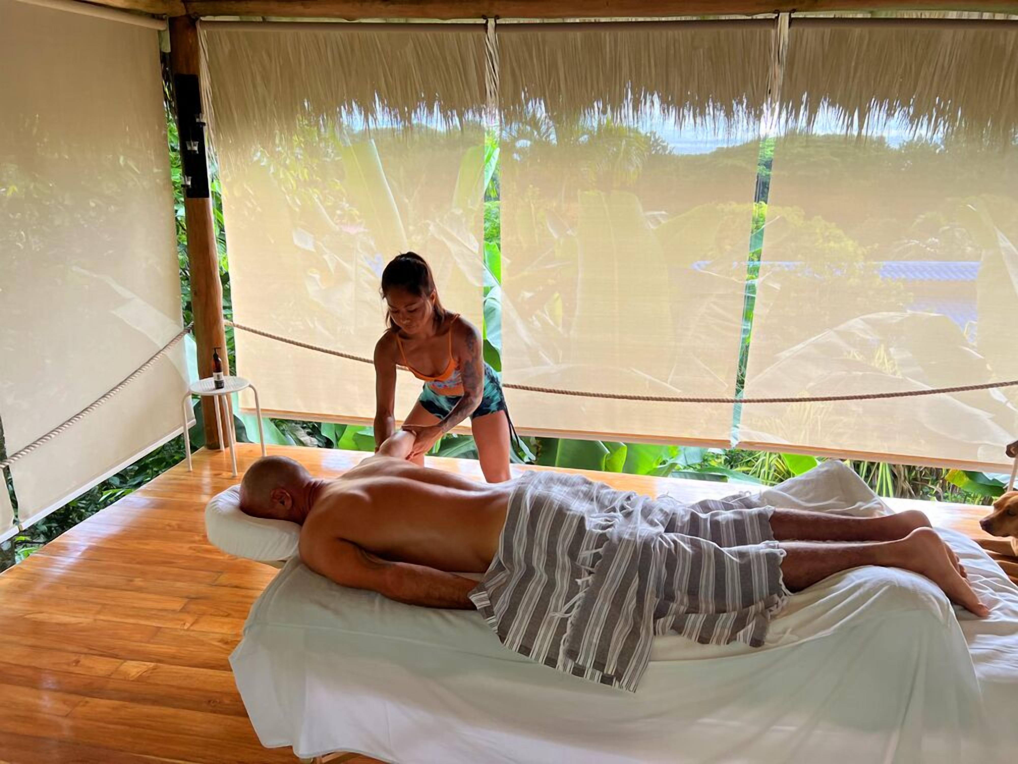 A massage therapy session in a room with a wooden floor and a bed covered with a white sheet.