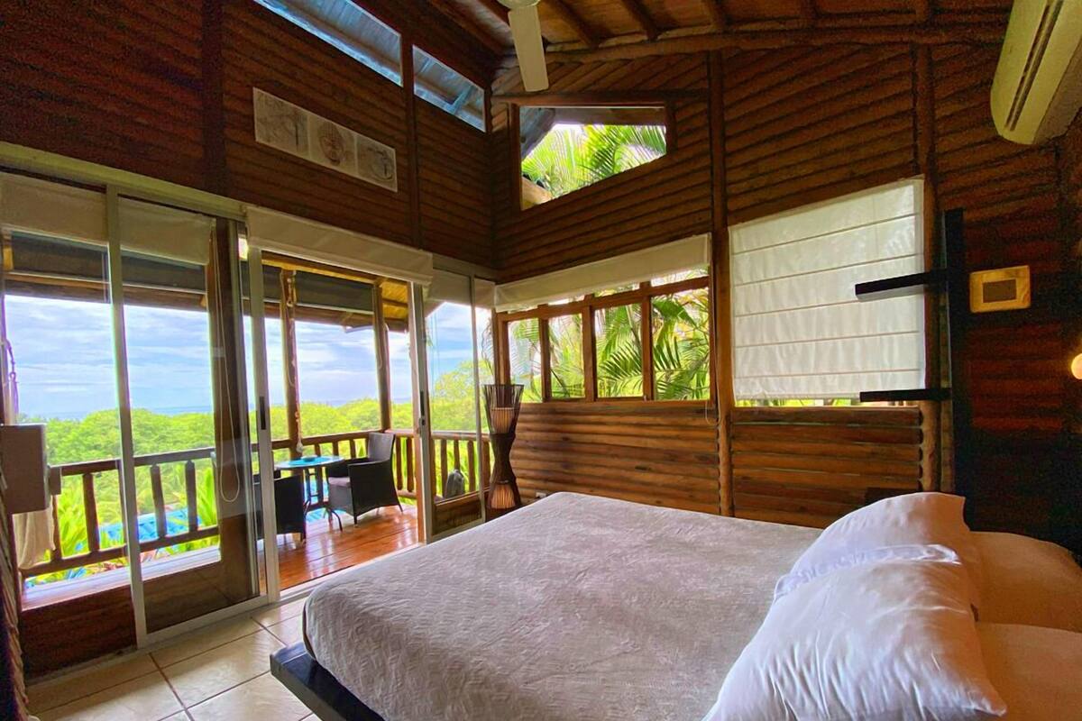Une chambre avec un grand lit, un balcon avec une table et des chaises, et une vue sur le paysage.