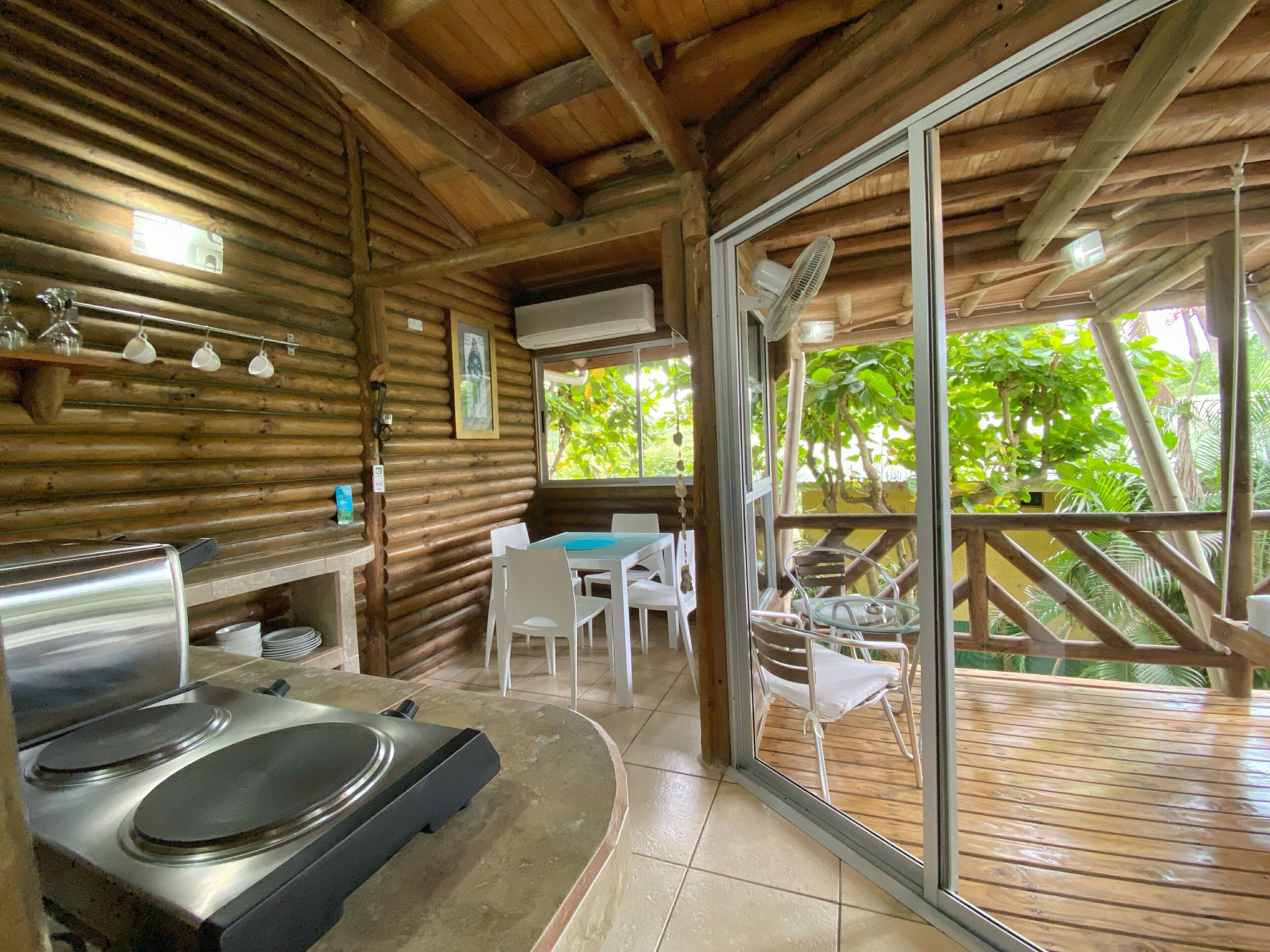 A wooden cabin with a kitchen area, a dining table with chairs, and a sliding glass door leading to an outdoor deck.