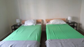 Two single beds with green and white bedding, wooden headboards, and nightstands with lamps.
