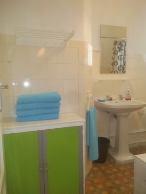 A bathroom with white tiled walls, a green cabinet, a sink with a mirror above it, and a patterned shower curtain.