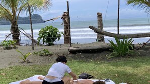 A beach scene with a person lying on a mat receiving a massage. - Miguel Surf  Camp (Quepos)