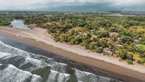 A coastal landscape with a sandy beach, dense greenery, and a river. - Miguel Surf  Camp (Quepos)