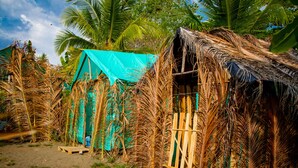 A rustic hut with a thatched roof, surrounded by palm fronds and a turquoise tarp. - Miguel Surf  Camp (Quepos)
