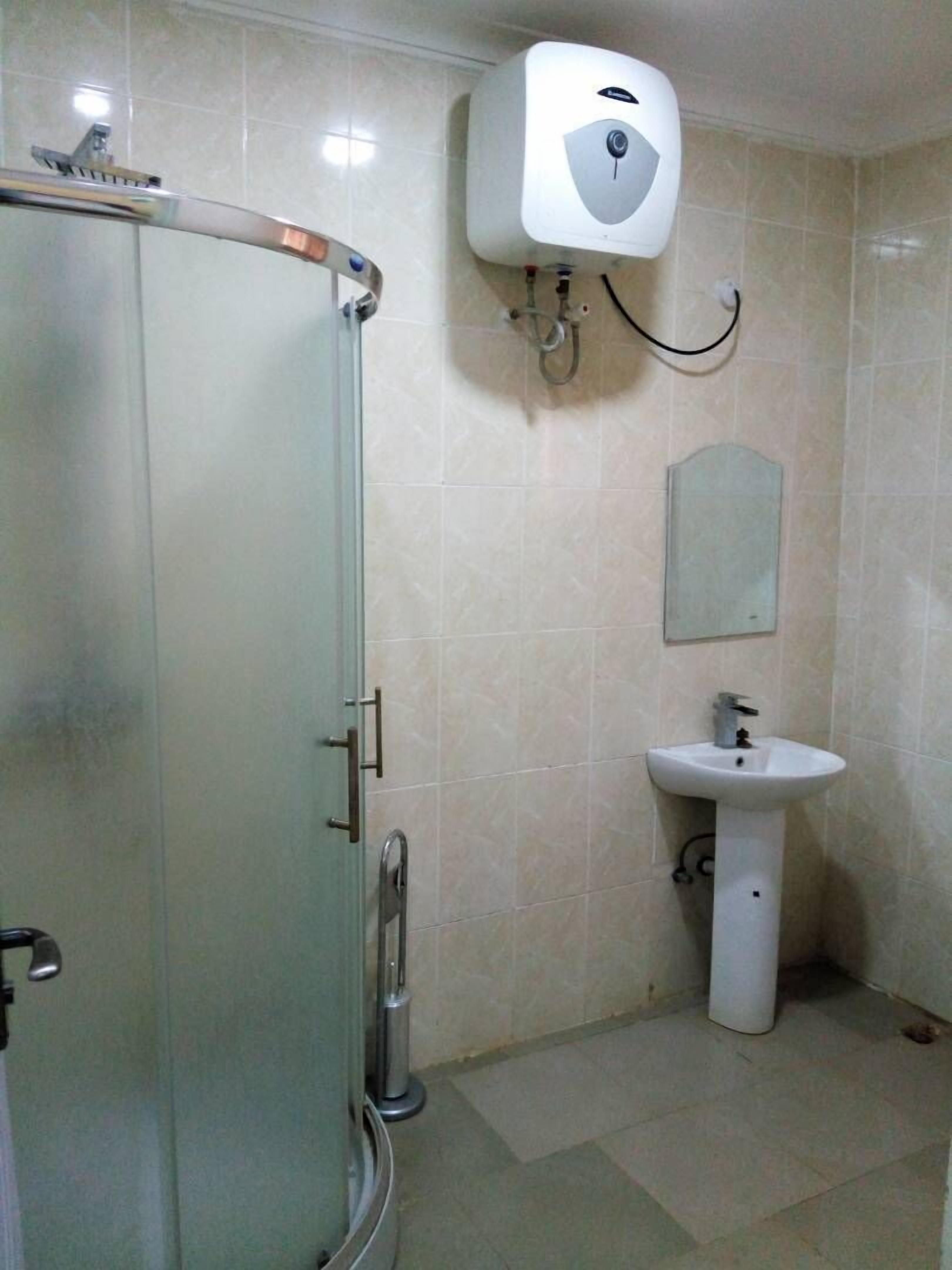 A bathroom with a glass shower enclosure, a wall-mounted hand dryer, and a pedestal sink.