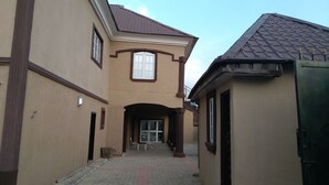 A building with a central entrance, a tiled roof, and a small courtyard with chairs. - DABOTOV Hotel and Suites (Ilorin)