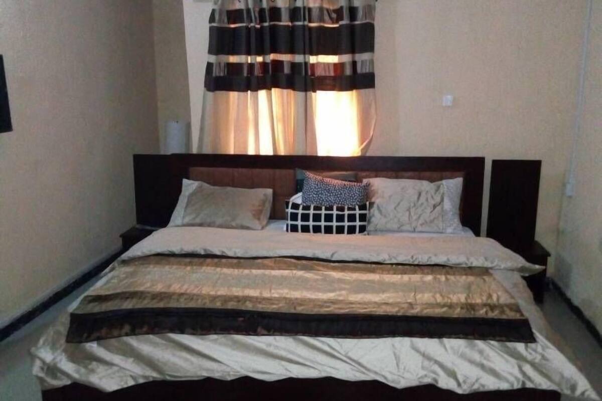 A bedroom with a bed, curtains, an air conditioner, and a floral rug.