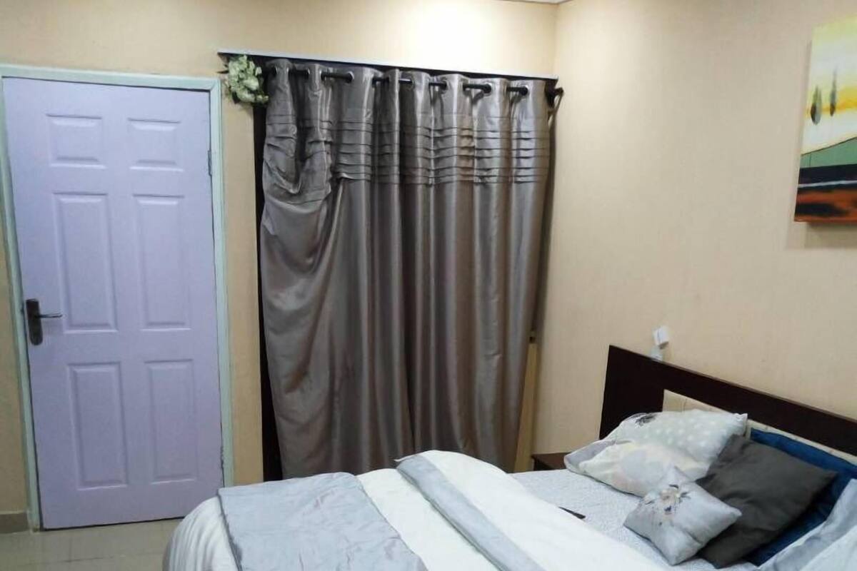 A bedroom with a bed, curtains, a door, and a wall-mounted painting.