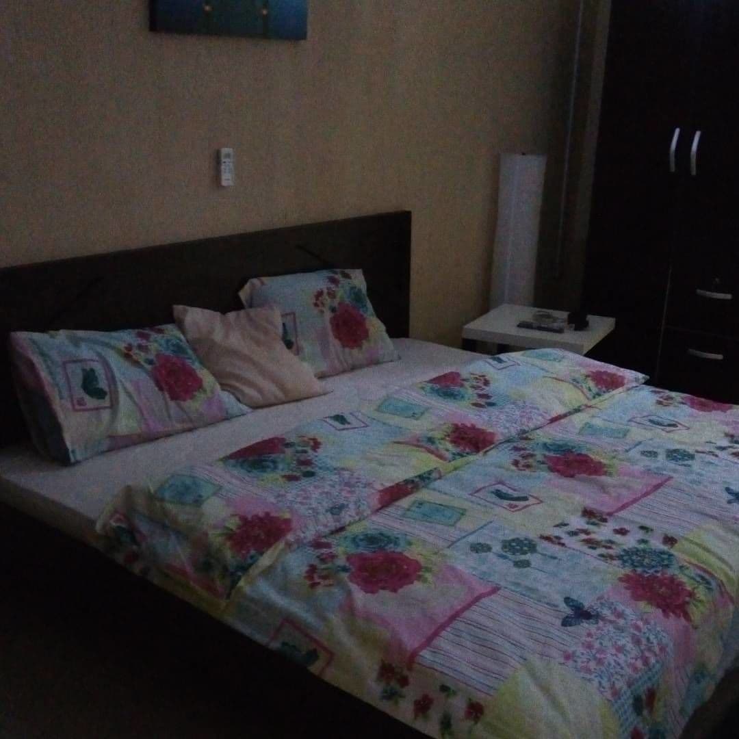 Una cama con colcha floral, una mesita de noche con lámpara y un armario.