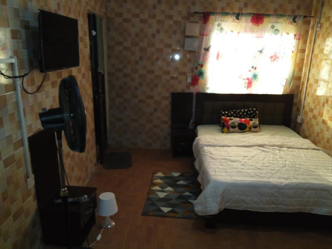 Quarto com cama, televisão na parede, ventilador e janela com cortinas.
