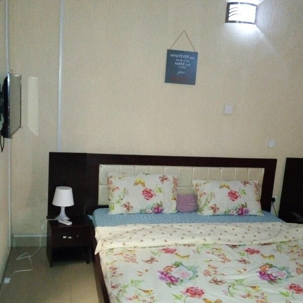Quarto com cama, mesa de cabeceira, abajur e placa na parede.