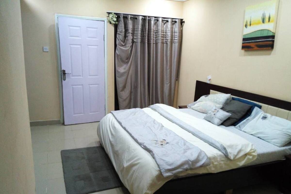 A bedroom with a bed, curtains, a door, and a painting on the wall.