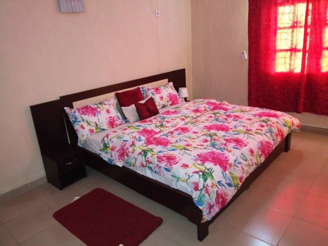 Una cama con ropa de cama floral, un plaid rojo y una mesita de noche.
