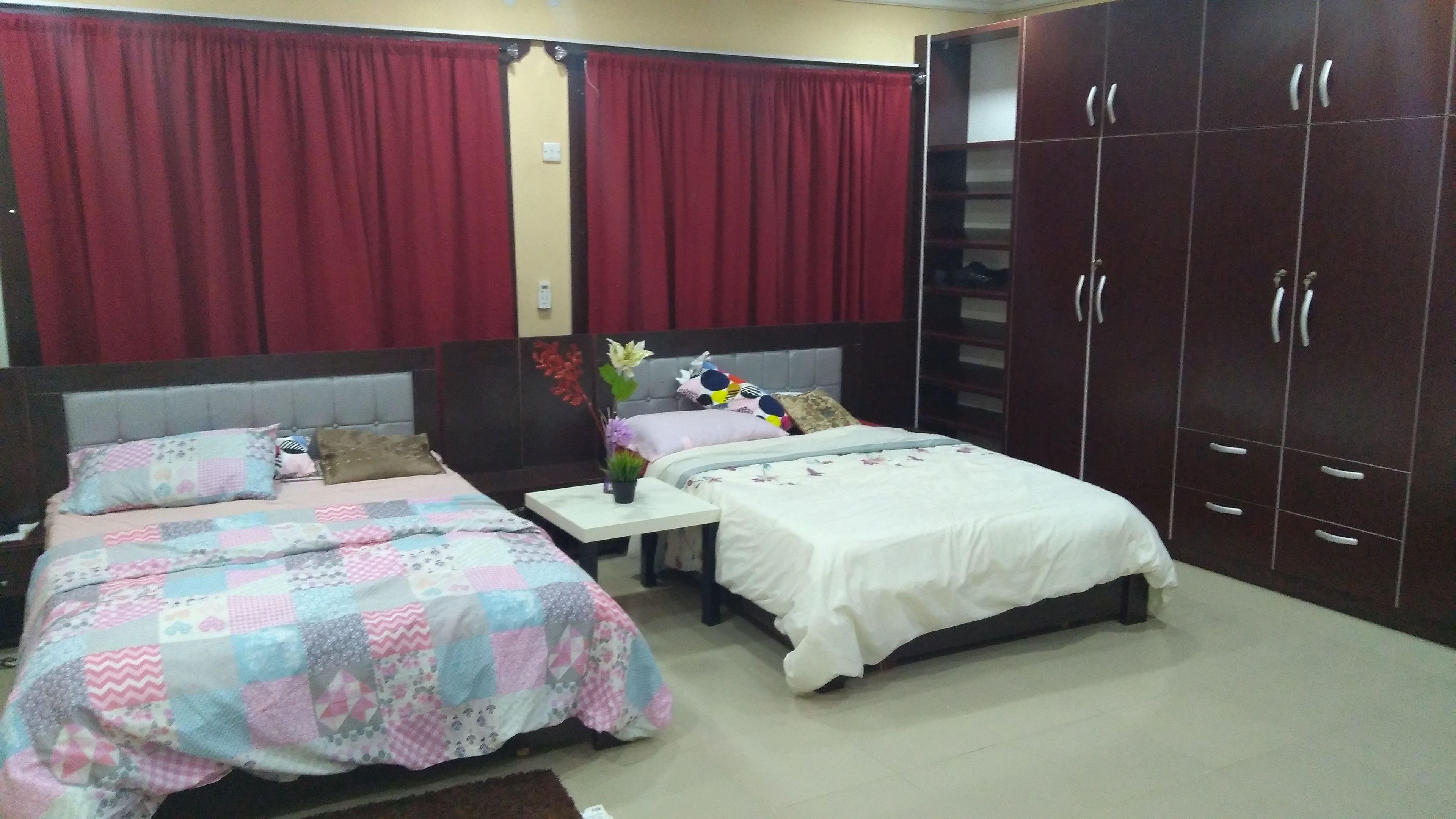 A bedroom with two beds, a nightstand, a wardrobe, and red curtains.