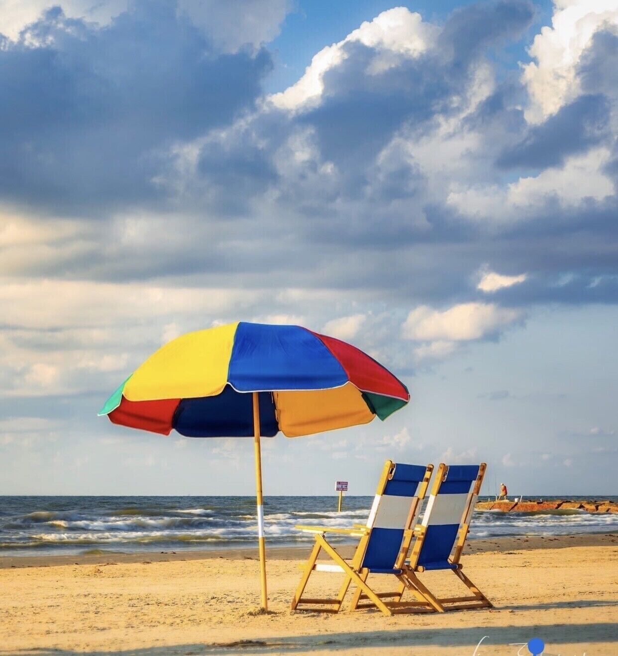 Une scène de plage avec un parasol coloré, deux chaises de plage et l’océan en arrière-plan.