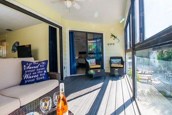 A sunlit porch with a sofa, two chairs, a bottle of wine, and a glass.