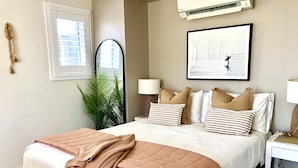 Un dormitorio con cama, mesitas de noche, un espejo, una planta en maceta y un cuadro en la pared.