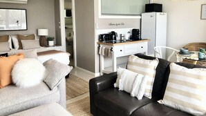 Un espacio habitable compacto con sofá, una mesita, kitchenette y baño a la vista a través de una puerta abierta.