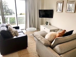 A living room with a sofa, a coffee table, a TV, and a view of the outdoors.