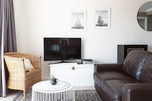 Una sala de estar con televisor, una silla de mimbre, un sofá de cuero y dos cuadros en la pared.