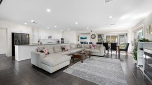 A modern living room with a sectional sofa, a coffee table, and a dining area with a table and chairs. - CYPRESS POINT LODGE - THE VINTAGE HOLIDAY HOUSES (POKOLBIN)