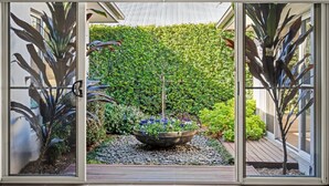 A garden with a central water feature, surrounded by a variety of plants and a wooden deck. - CYPRESS POINT LODGE - THE VINTAGE HOLIDAY HOUSES (POKOLBIN)