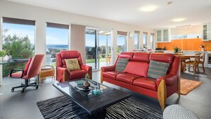 Un salon moderne avec un canapé en cuir rouge, une table basse en verre et un coin repas doté de meubles de rangement orange.