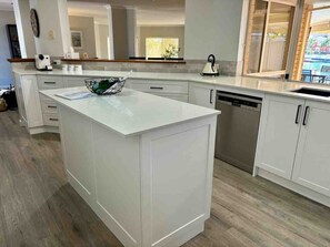 A modern kitchen with white cabinetry, a central island, and a dishwasher. - Dockside on Mandurah Canals (Mandurah)