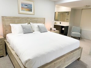 A bedroom with a wooden bed, a bedside table, a chair, a mirror, and a bathroom visible in the background. - Dockside on Mandurah Canals (Mandurah)