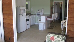 Una cocina compacta con electrodomésticos blancos, una pequeña zona de comedor con un taburete de bar y fachada de madera.