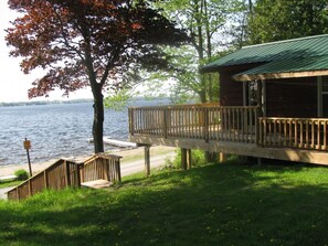 A lakeside cabin with a wooden deck and a green roof overlooking a body of water. - Cedar Cottage at Shiloh Cottages - Fenelon Falls (Fenelon Falls)