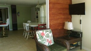 Una sala de estar con una silla de mimbre, un televisor y un comedor al fondo.