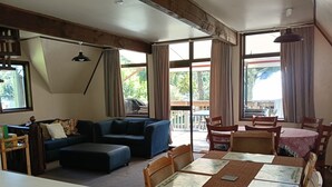 Una sala de estar con sofá, reposapiés, mesa de comedor, sillas y vistas al exterior a través de amplios ventanales.