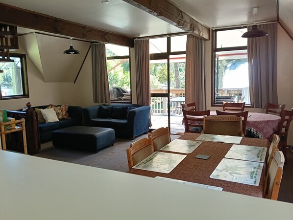 A living room with a sofa, ottoman, dining table, chairs, and a view of the outdoors through large windows.