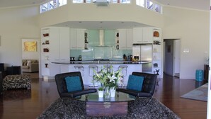 Una cocina moderna con armarios blancos, una isla central y una zona de comedor con dos sillas y una mesa de vidrio.