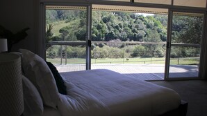 Un dormitorio con un amplio ventanal corredera que da a un balcón con vistas a un paisaje boscoso.