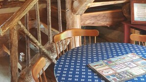 Un intérieur rustique en bois, avec un escalier en colimaçon, des chaises en bois et une table recouverte d’une nappe à motifs.
