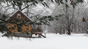Une cabane en bois dotée d’un porche, entourée d’arbres couverts de neige.