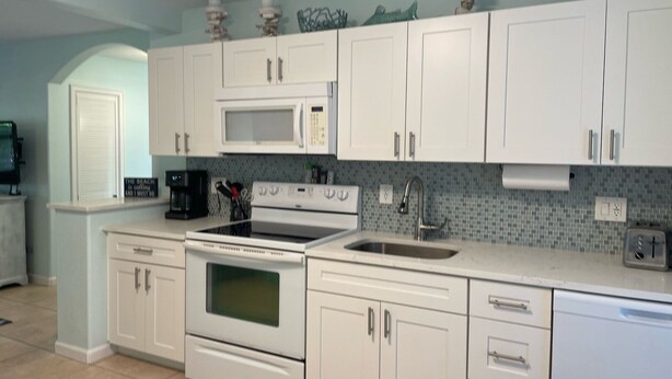 A kitchen with white cabinets, a microwave, a stove, and a sink.