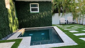 A swimming pool with a geometric tile border, surrounded by a neatly trimmed lawn and a hedge wall.